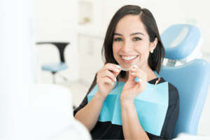 Woman with dark hair holding a clear aligner while in an orthodontist chair