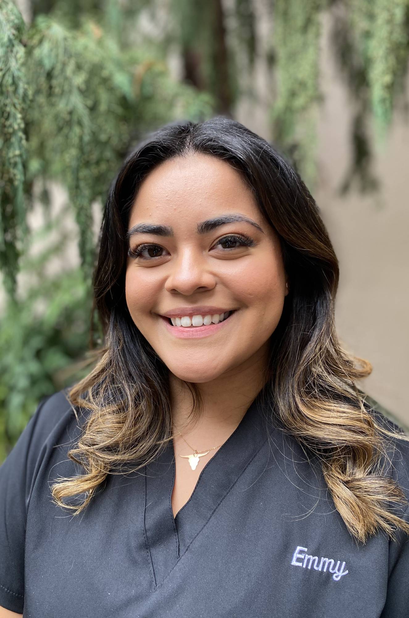 Professional headshot of Emma, Laidlaw Orthodontics team member, smiling outdoors with greenery backdrop.