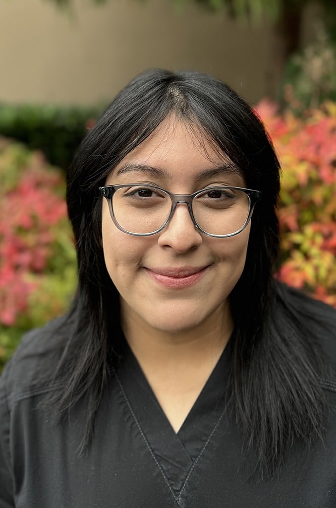 Woman wearing glasses smiling at camera with colorful flowers in background