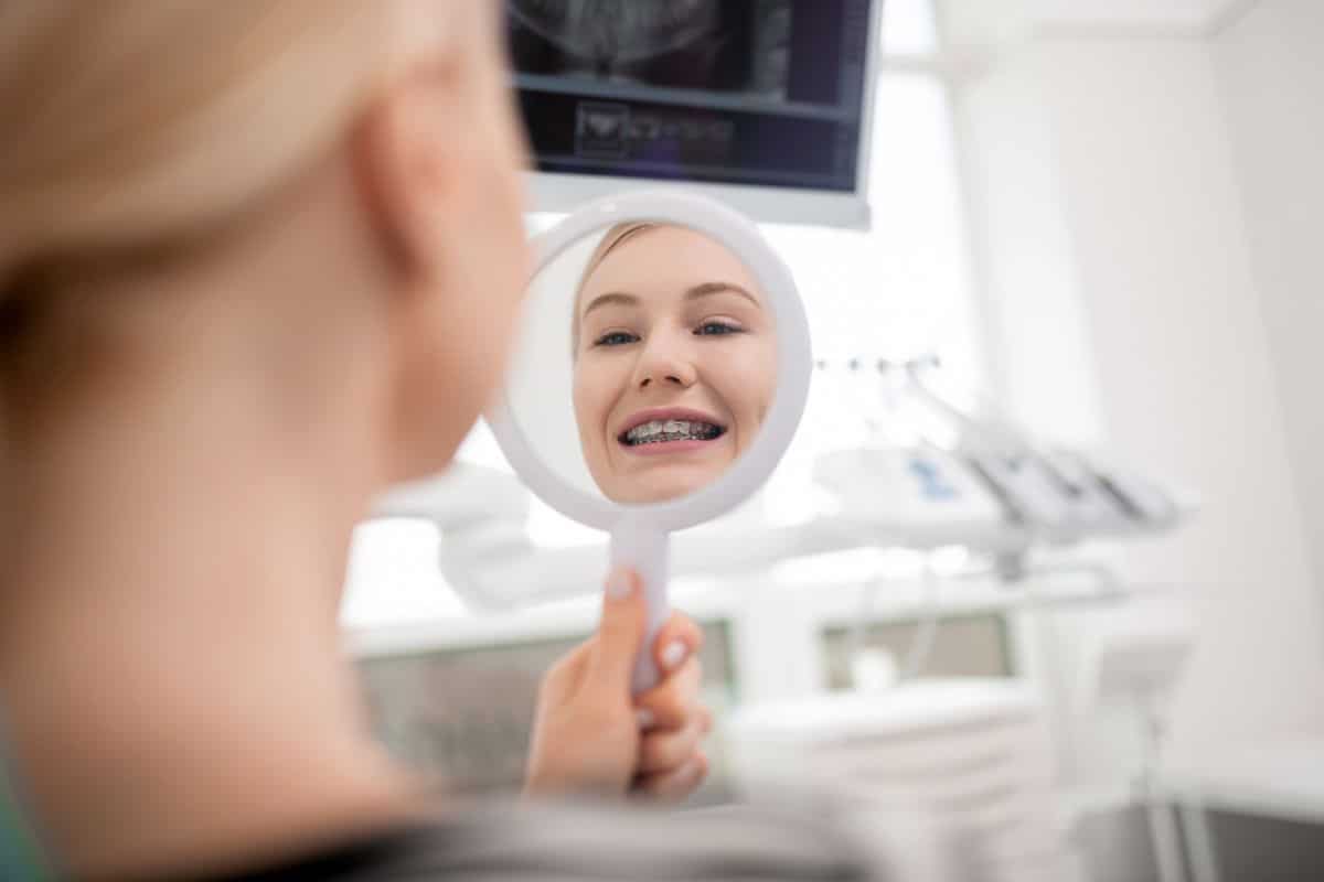 Woman checking clean and stain-free clear braces in dental mirror